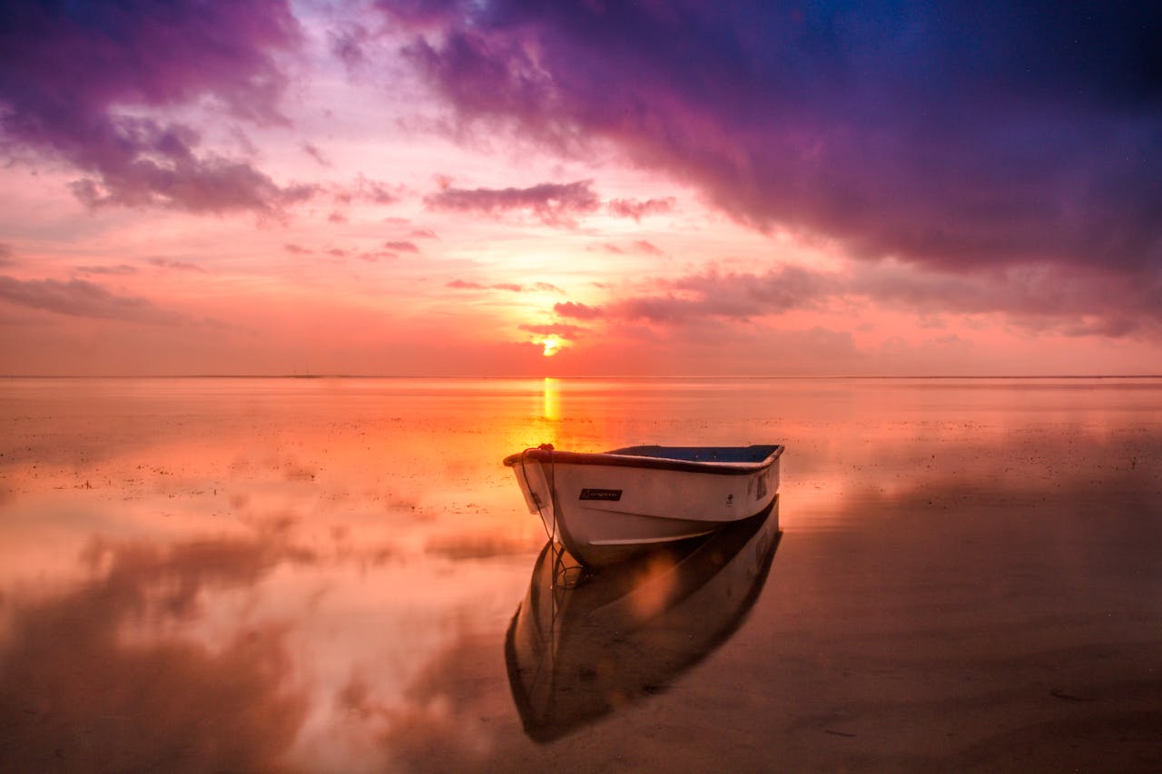 A tranquil scene of a boat at sunset with vivid sky reflecting on calm waters.